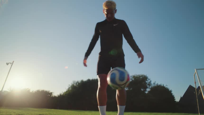 Cinematic low-angle slow-motion footage shows a skilled football player juggling the ball with his feet on a green pitch