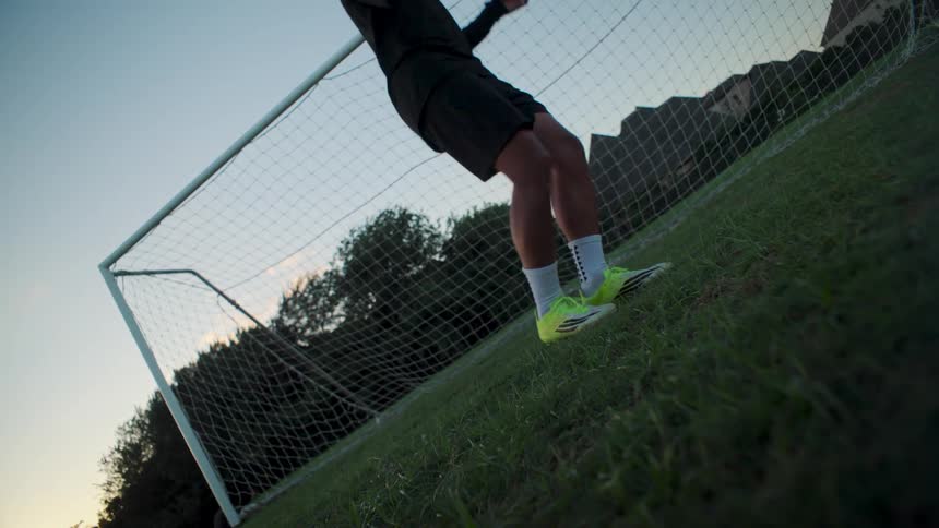 Slow motion low angle shot of a soccer player juggling a ball in front of the goal at dusk
