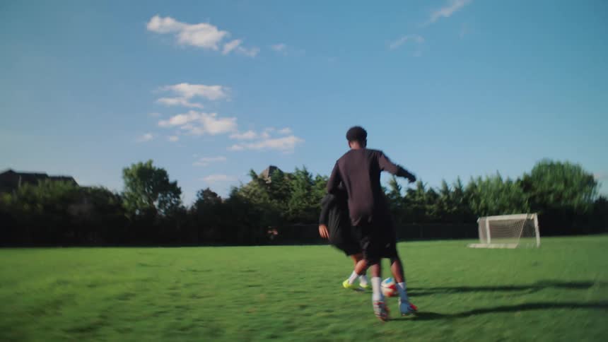 Energetic slow-motion footage captures two young men engaged in a one-on-one soccer practice on a sunny grass field