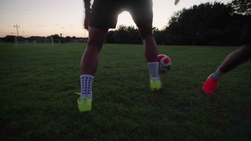 A close-up slow-motion shot of two soccer players' feet practicing dribbling drills on a grassy field at dusk