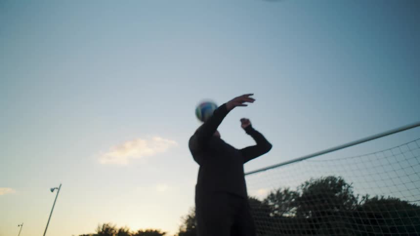 A skillful male soccer player juggles a ball with his feet, knees, and head in slow motion on a grass field at sunset