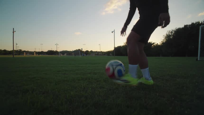 A young soccer player juggles the ball with expert skill on a field at dusk, filmed in dramatic slow motion