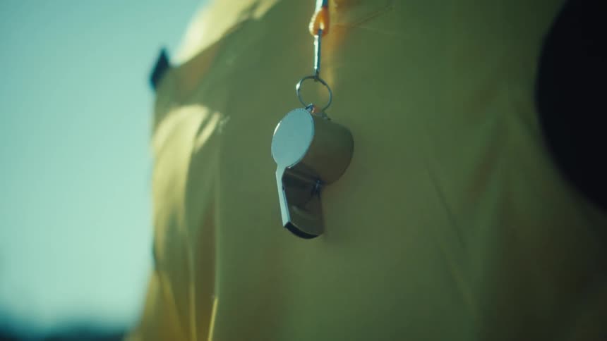 A dramatic close-up of a whistle hanging on a yellow jacket with a bright sun flare