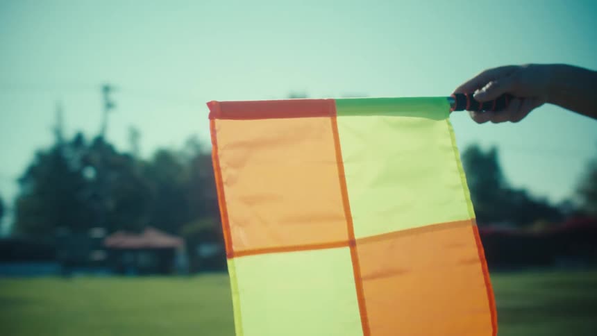 In slow motion, a soccer referee's hand raises a checkered flag to signal a call during a game