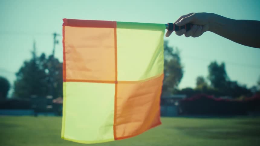 A slow-motion close-up of a soccer linesman's flag being raised on a sunny day