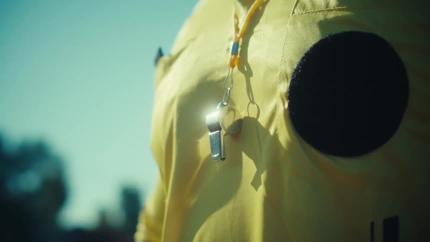 The sun gleams off a silver whistle hanging on the yellow jersey of a sports referee