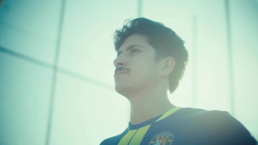 Low angle shot pans up to a determined young soccer player with a mustache holding a ball on a sunny urban court