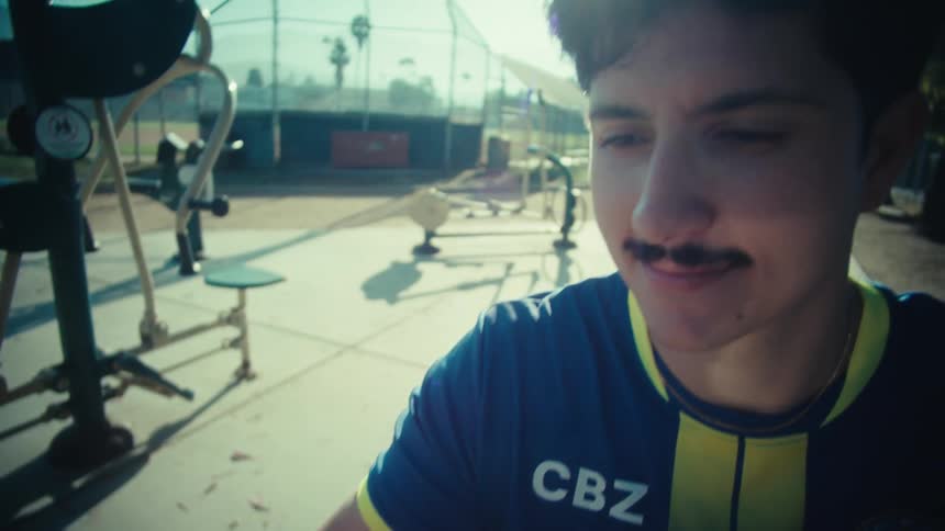 Close-up of a young man in a soccer jersey looking at his smartphone while sitting at an outdoor park gym