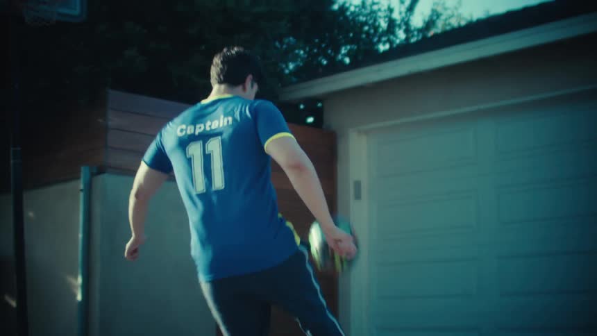 A talented young soccer player juggles a ball in slow motion in a sunny urban alley