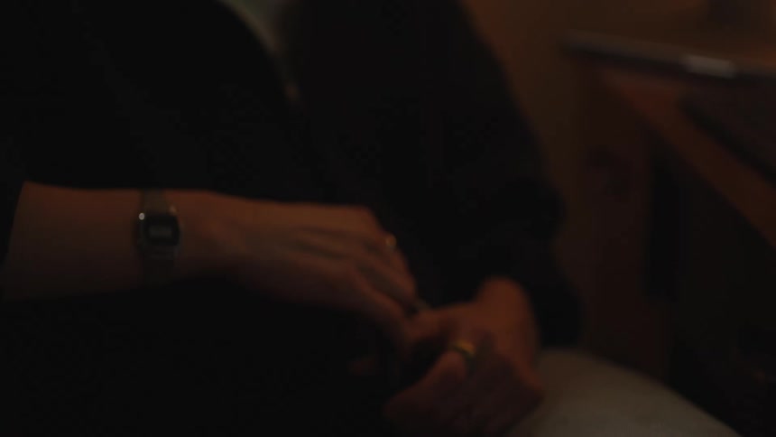 A slow-motion close-up of a person's hands fidgeting with a pen while sitting at a desk in a dimly lit room