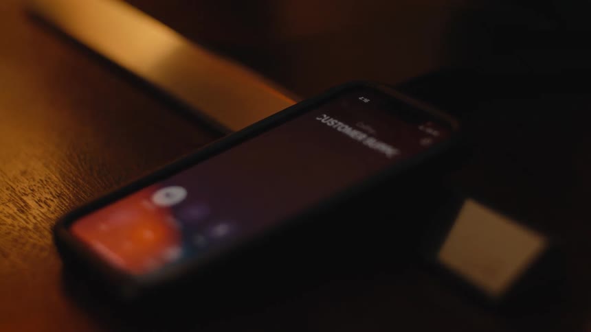 A close-up shot captures a person calling US customer support on their smartphone in a dark, atmospheric setting