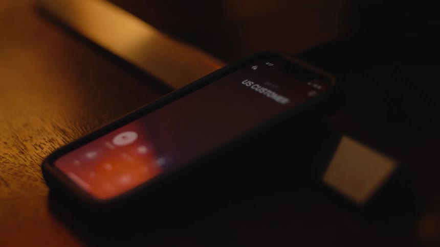 A smartphone on a dark surface displays a live transcription of a phone call, identifying the caller as 'US Customer Support'