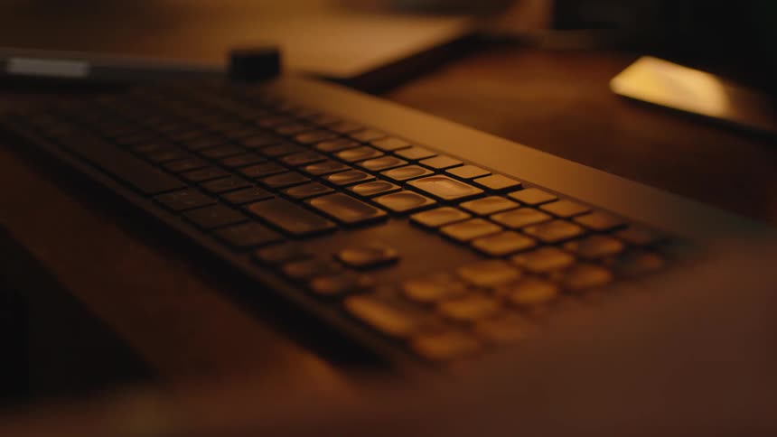 A graphic designer's hand glides a stylus across a drawing tablet in a warmly lit, moody home office at night