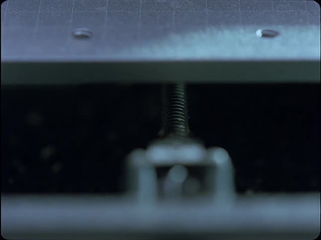 A close-up view of a metal threaded screw slowly rotating on a piece of industrial machinery