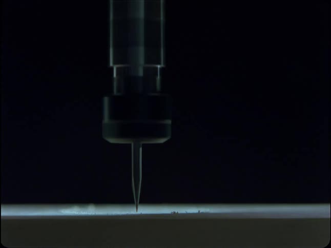 A macro close-up of a high-precision CNC machine bit engraving a line onto a flat surface in the dark