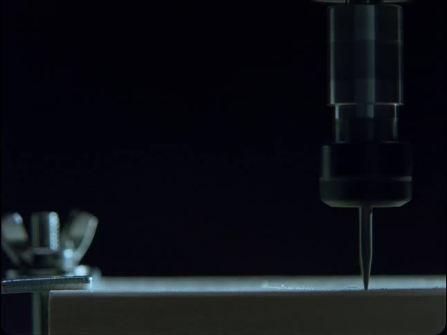 A high-speed precision milling bit carves into a white material, sending fine shavings flying against a black background