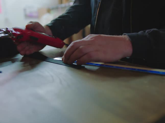 A worker precisely cuts a black synthetic strap with a hot knife, which melts and seals the edge as smoke rises in slow motion