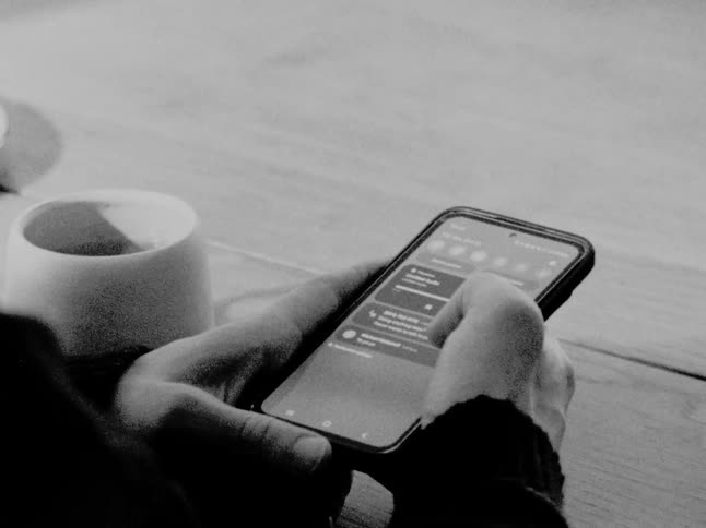 Close-up, black and white footage shows a person holding a smartphone and scrolling through their notifications