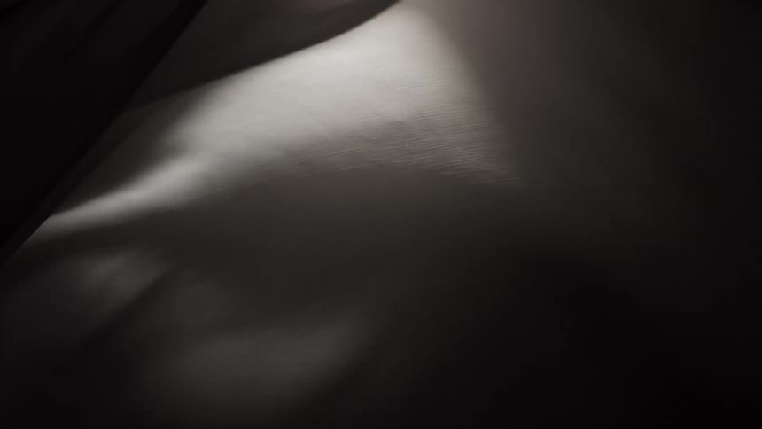 A close-up shot of dark, elegant fabric moving in slow motion, creating abstract waves and shadows against a black background