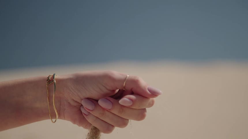 Slow motion close-up of fine sand slipping through a woman's hand at the beach