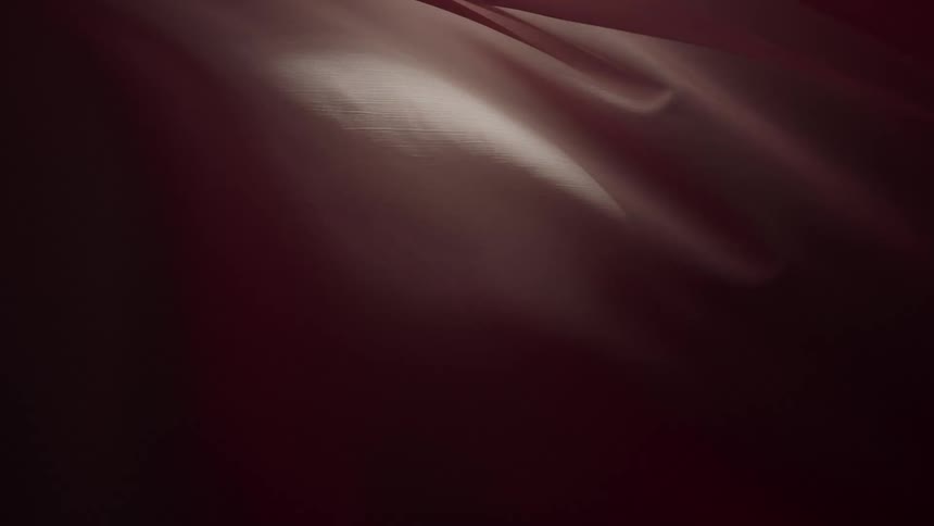 An elegant and abstract background of dark maroon silk fabric flowing gently in slow motion