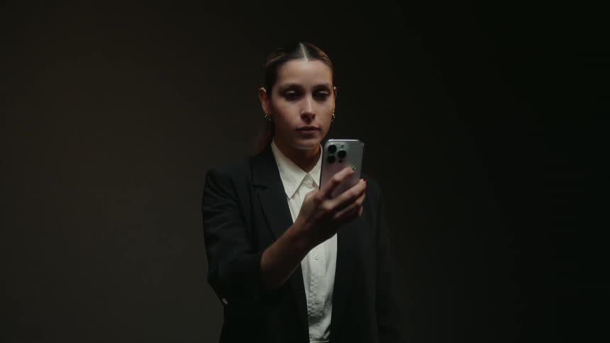 A businesswoman in a suit uses her smartphone while standing in a dimly lit studio