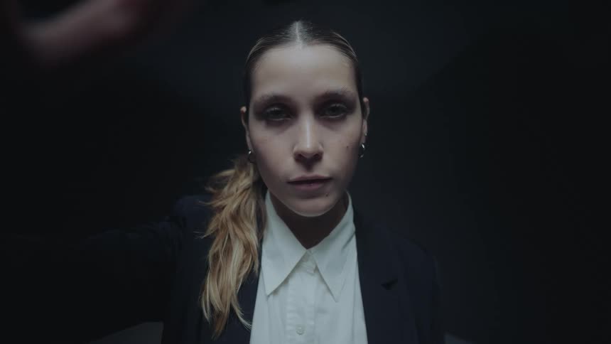 POV shot of a finger swiping across a virtual interface in front of a serious businesswoman in a dark, spotlit room