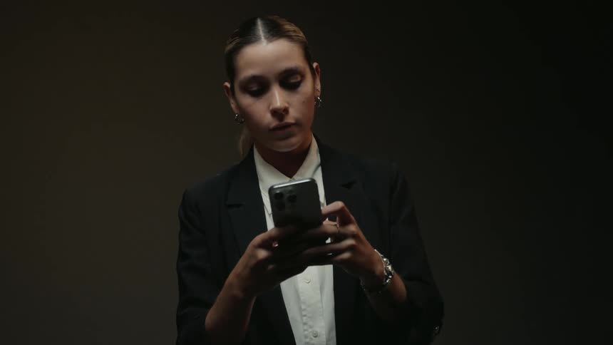 Slow zoom on a serious businesswoman in a dark setting, intently using her smartphone