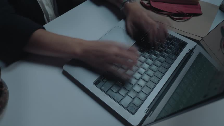 High-angle timelapse of hands typing furiously on a laptop keyboard while working late
