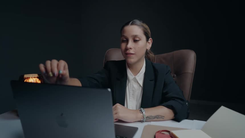 A stylish businesswoman in a dark office slowly opens her laptop and smiles as she begins to work