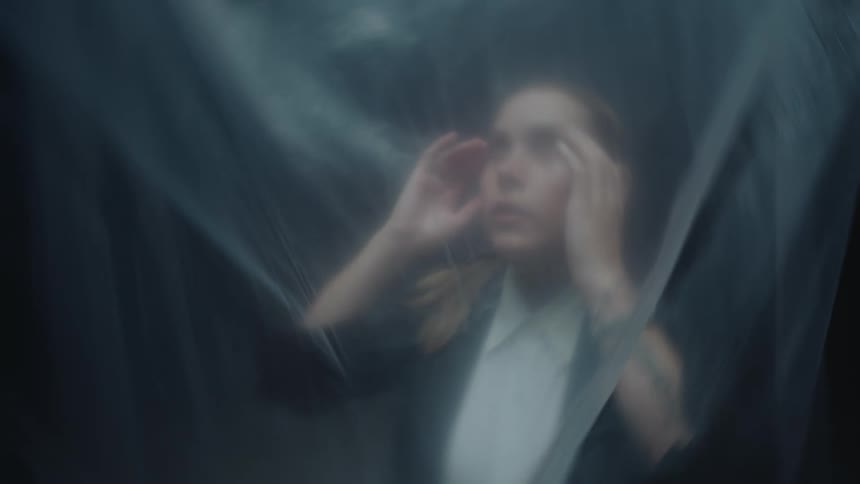 A distressed woman in business attire presses against a translucent plastic sheet, feeling trapped and isolated