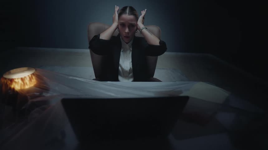 Anxious businesswoman holds her head in despair in a dark, abandoned office where the furniture is covered in plastic sheeting