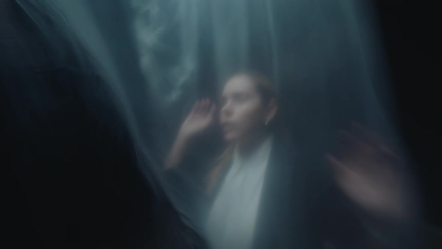 A blurry, artistic shot of a distressed woman trapped behind a translucent plastic sheet, conveying a sense of anxiety and isolation