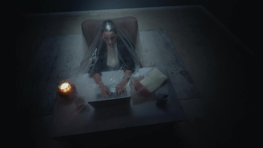 Conceptual high-angle shot of a woman working on a laptop at night, isolated and trapped under a plastic sheet