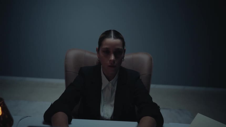 The camera dramatically zooms out from a stressed businesswoman to reveal her working alone late at her desk in a dark, empty room