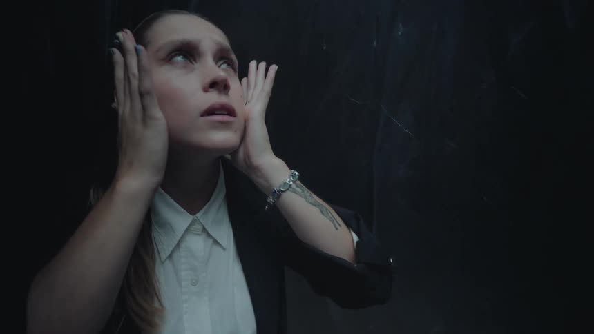 A young businesswoman experiences anxiety and fear, holding her head in a dark, claustrophobic space in slow motion