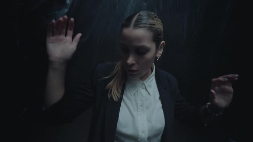 A scared woman in a business suit moves slowly through a dark, claustrophobic space in slow motion