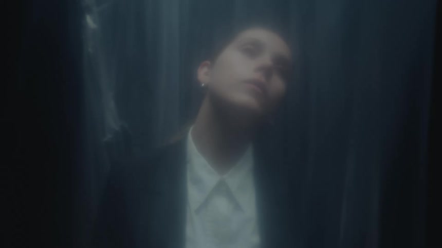 An out-of-focus shot of a young businesswoman with closed eyes, slowly tilting her head back in a dreamlike, hazy atmosphere