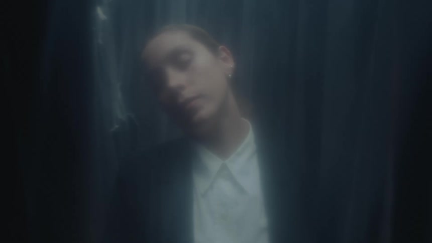 A blurry, artistic close-up of a person with closed eyes lowering their head in a dark, moody environment with soft lighting