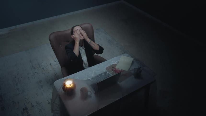 High-angle shot of a tired and stressed businesswoman rubbing her eyes while working late at night in a dimly lit, empty office