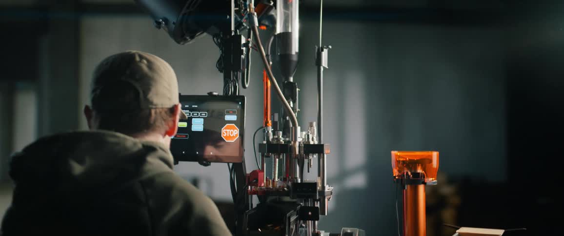 A man operates a sophisticated automated bullet reloading machine using a touchscreen tablet in a workshop