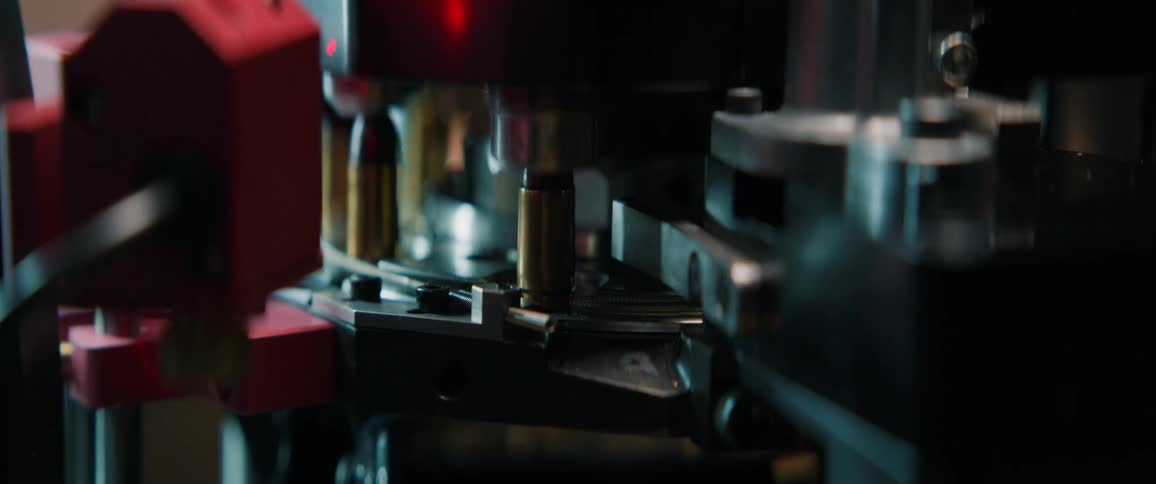 A slow-motion close-up shows an automated machine assembling bullets on a factory production line