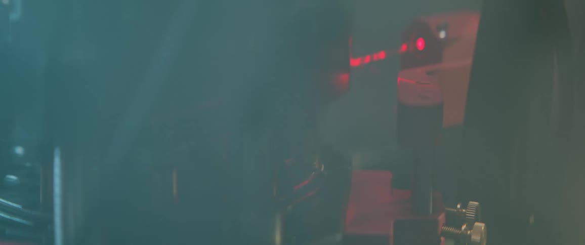 Mysterious smoke clears to reveal a sophisticated red laser experiment operating in a high-tech laboratory