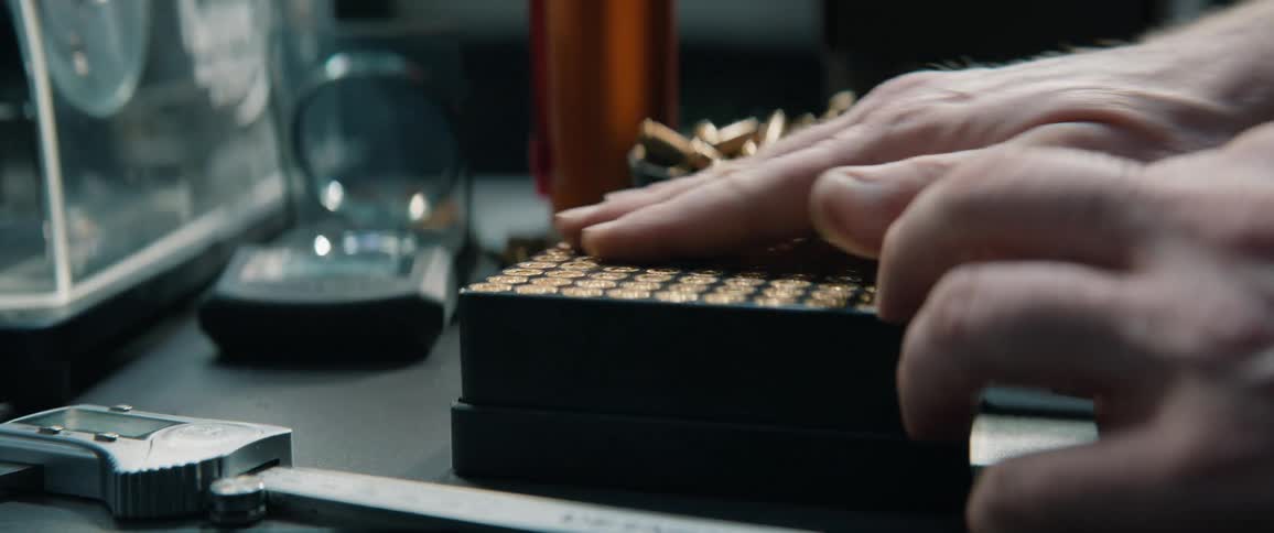 A person carefully organizes bullet casings into a reloading tray on a workbench full of reloading equipment