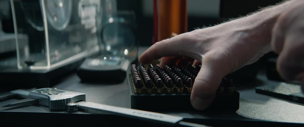 Man opens a box of newly made bullets, carefully inspecting them in his workshop