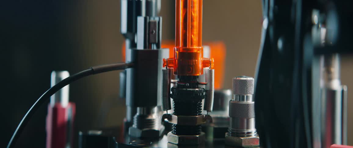 A dramatic close-up tilt-down reveals an automated ammunition reloading press in operation