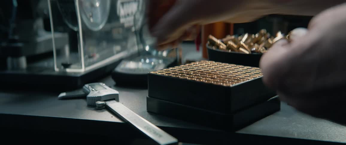 Close-up of a person reloading ammunition, carefully placing bullets into a tray before measuring one with a digital caliper