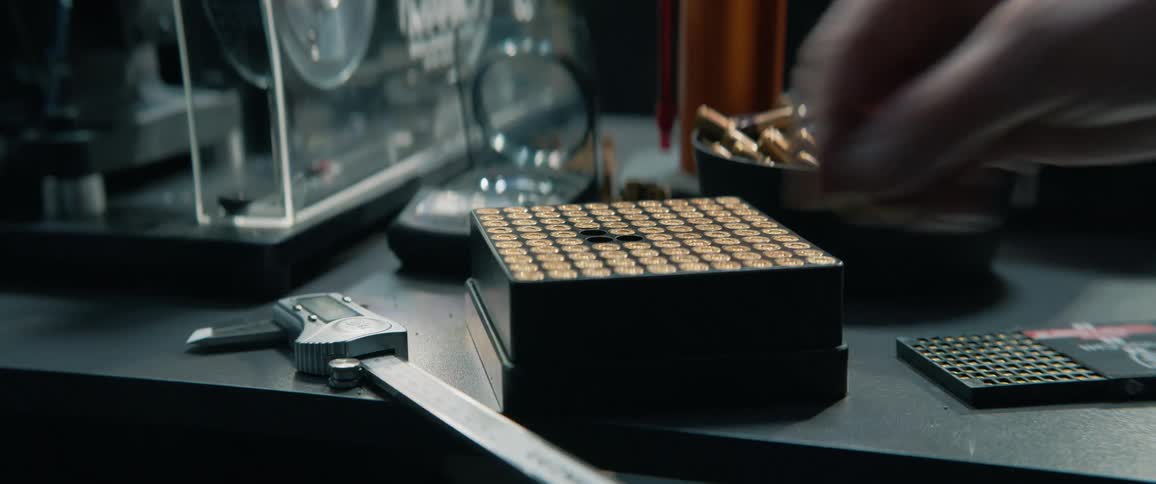 A person carefully organizes handgun ammunition, placing bullets one by one into a reloading tray on a workbench