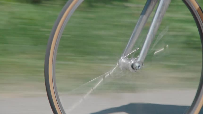 Slow-motion side profile of a bicycle's wheel and pedals in motion along a sunny path