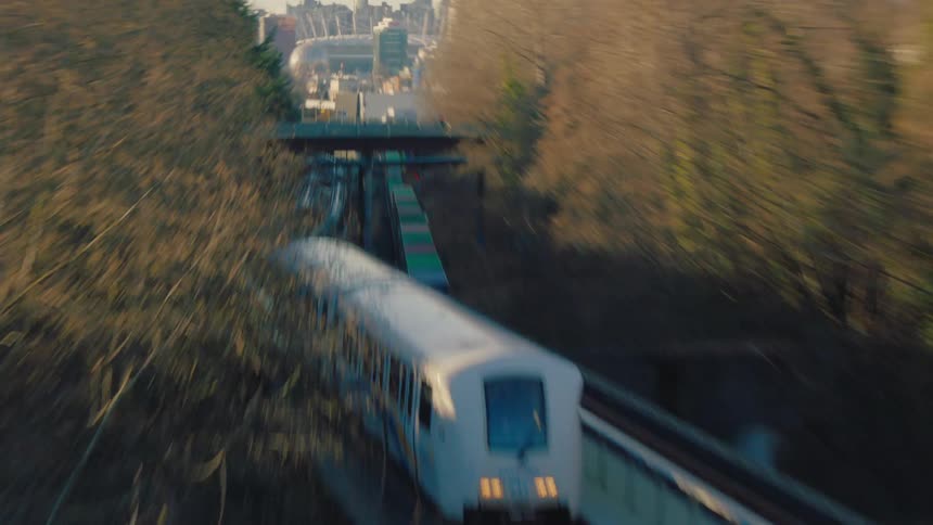 A dynamic pull-back shot reveals a SkyTrain traveling along an elevated track, leaving the Vancouver skyline with BC Place stadium in the distance